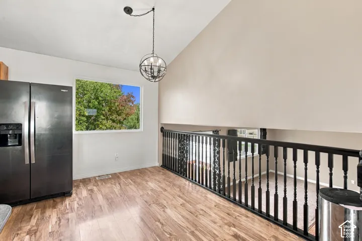 Vaulted ceilings, wood-finish flooring, matte black metal spindle railing, sphere-style pendant lighting, and a window with exterior greenery