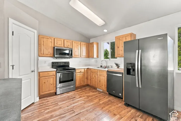Kitchen featuring wood cabinetry, stainless steel appliances, wood-finish flooring, and a double-basin sink