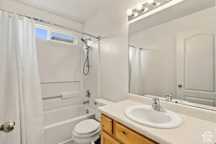 Bathroom featuring a wood vanity with a solid-surface countertop, an oval undermount sink, a chrome-finish faucet, a large wall-mounted mirror, and a combination tub and shower with a handheld spray fixture
