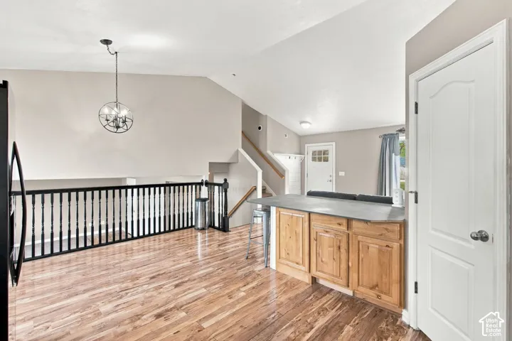Vaulted ceilings, wood-finish flooring, built-in kitchen cabinetry with a solid surface countertop, and a decorative metal chandelier