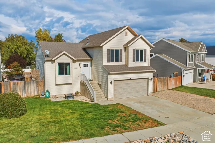 Split-level residence featuring light-colored horizontal siding, asphalt shingle roofing, concrete driveway, attached two-car garage, and a wood-fenced rear yard
