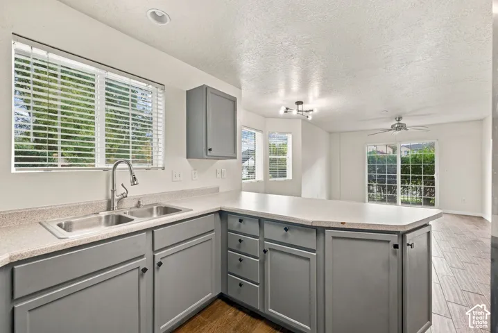 Kitchen featuring gray cabinetry, solid surface countertops, a stainless steel dual-basin sink with a pull-down faucet, wood-finish flooring, and recessed ceiling lighting