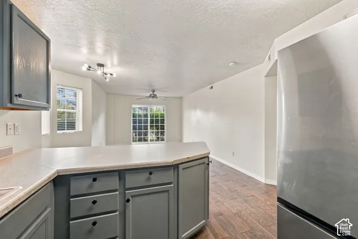 Kitchen featuring gray cabinetry, neutral countertops, stainless steel refrigerator, wood-finish flooring, and multi-light ceiling fixture