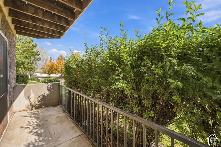 Covered concrete balcony with stone-accented exterior wall, metal railing, and mature shrubbery