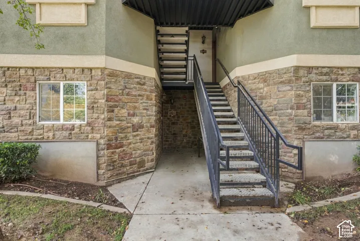 Exterior facade featuring stone veneer masonry, stucco siding, dual-level metal staircase with handrails, and concrete entryway