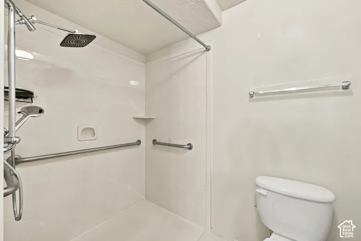Shower featuring a dual-head rainfall and handheld sprayer system, integrated wall-mounted grab bars, built-in shelving, and a white toilet