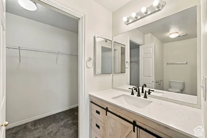 Vanity featuring a light wood-finish sliding barn door cabinet, white stone countertop with an integrated basin, oil-rubbed bronze faucet, and a large-format vanity mirror with integrated multi-bulb lighting