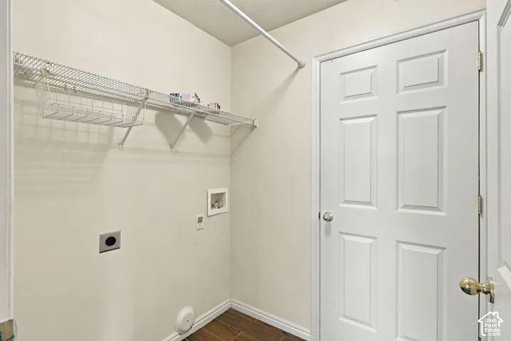Utility room featuring wood-finish flooring, white six-panel door, metal wire shelving with integrated basket, and dedicated wall-mounted plumbing and venting connections