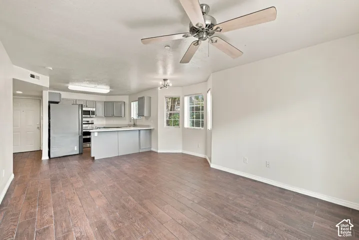 Open-concept area featuring wood-finish flooring, a kitchen peninsula, stainless steel refrigerator, multi-pane bay window, and a ceiling fan