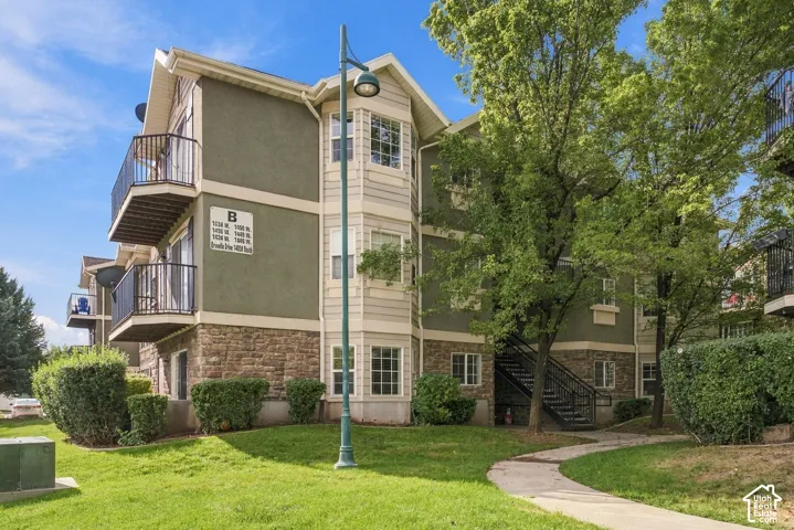 Multi-story building exterior featuring stone masonry cladding, stucco siding, dual private balconies with metal railings, and a peaked roofline