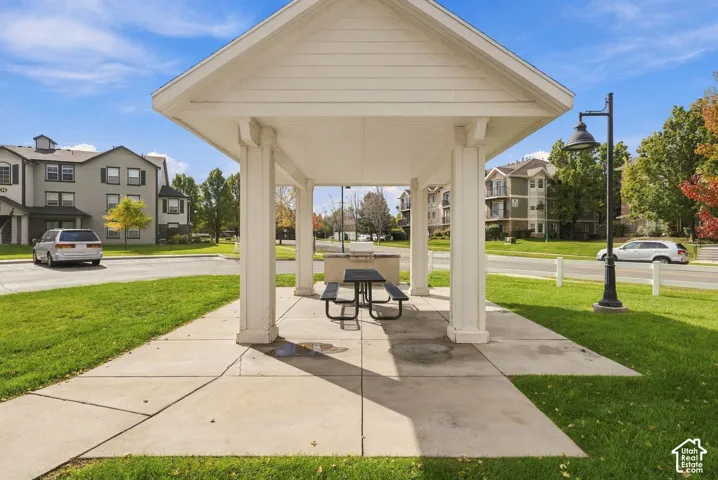 Covered outdoor pavilion featuring structural columns, a concrete pad, a built-in stone grill, and a pedestal-mounted light fixture