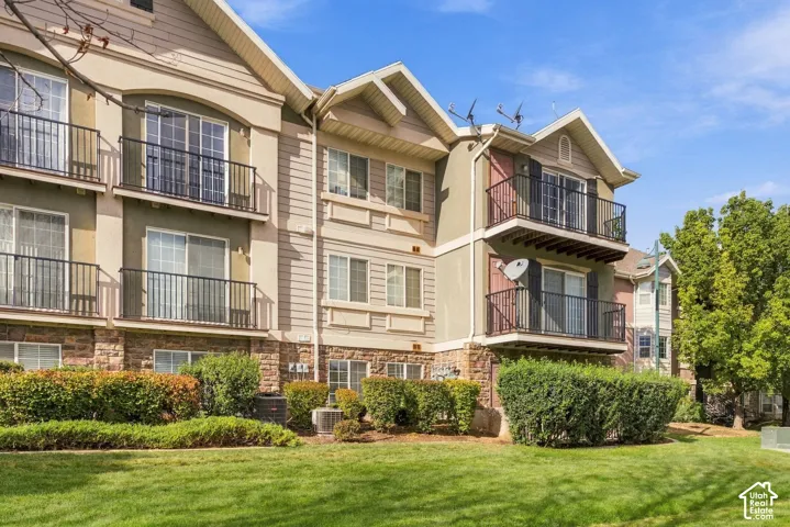 Multi-story residential building exterior featuring stone masonry cladding, horizontal siding, private railed balconies, and landscaped grounds