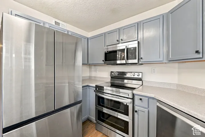 Kitchen featuring blue shaker-style cabinetry, stainless steel appliances, a double-oven range, stone-composite countertops, and wood-finish flooring