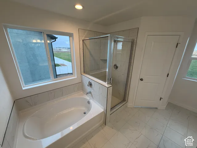 Soaking tub with tile surround, glass-enclosed shower, large-format tile flooring, and recessed lighting