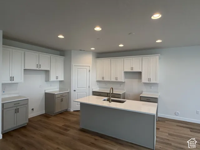 Kitchen featuring white upper cabinetry, grey lower cabinetry, white quartz countertops, central island with an undermount sink, and wood-finish flooring