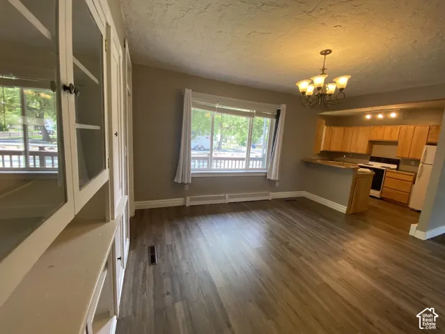 Wood-finish flooring, built-in glass-front cabinetry, neutral wall paint, multi-light chandelier, and wooden kitchen cabinetry with breakfast bar