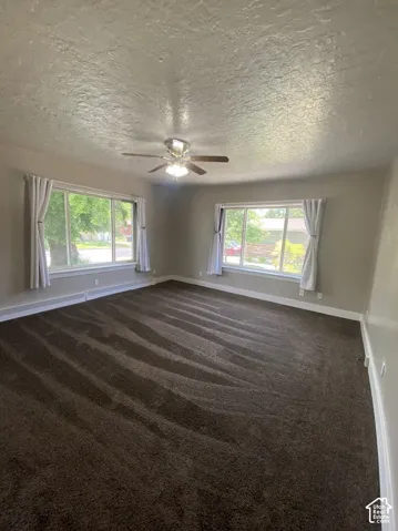 Room featuring textured ceiling, carpeted flooring, two large windows, and a multi-light ceiling fan