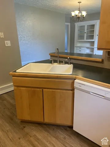 Kitchen area featuring a white double-basin sink with a gooseneck faucet, dark countertops, light wood cabinetry, integrated white dishwasher, and built-in white glass-front hutch