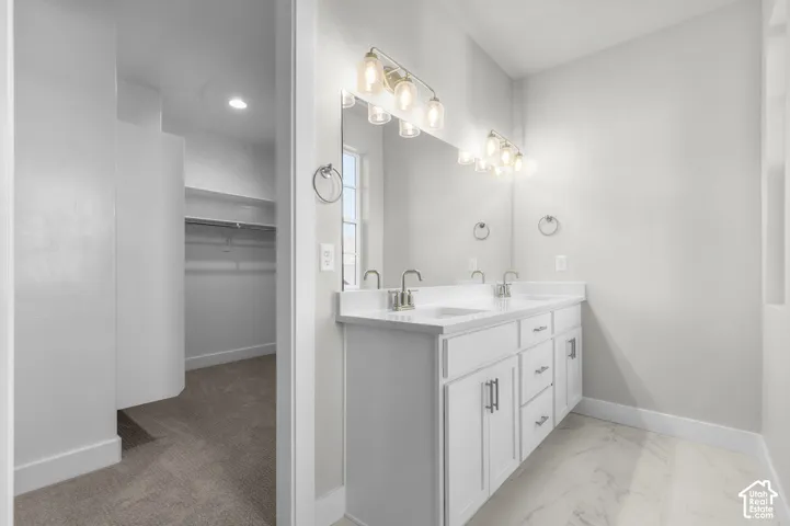 Dual-sink vanity with white cabinetry, stone-surface countertop, full-width mirror, polished chrome hardware, and patterned tile flooring