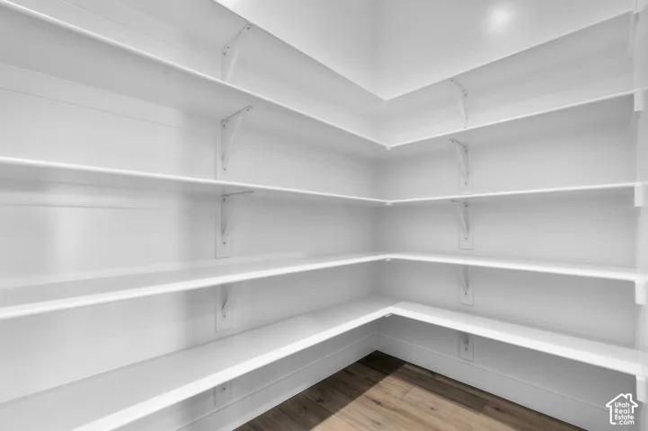 Walk-in pantry featuring white wrap-around shelving with bracket support and wood-finish flooring