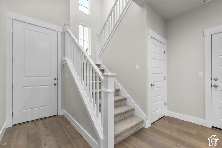 Foyer featuring high ceilings, stacked windows, wood-finish flooring, a carpeted staircase with white railings, and paneled doors