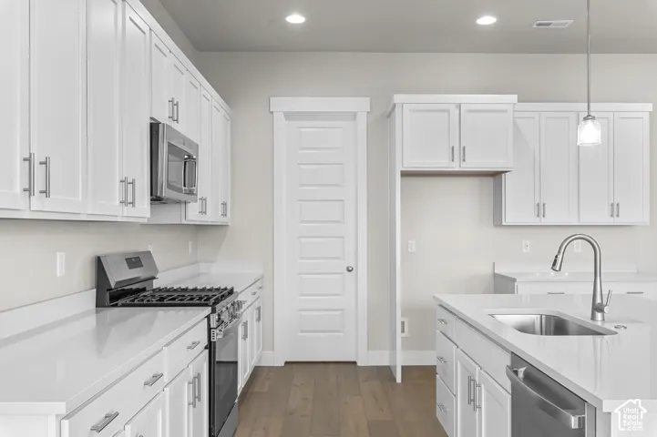 Kitchen featuring white shaker-style cabinetry, quartz countertops, stainless steel appliances, a central island with an undermount sink, and wood-finish flooring