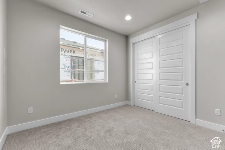 Neutral-toned room featuring wall-to-wall carpeting, white sliding closet doors with paneled detailing, and a double-pane window