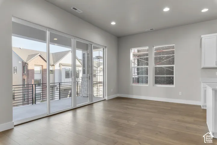 Wood-finish flooring, recessed lighting, multi-panel sliding glass doors, covered deck with metal railing, and white cabinetry