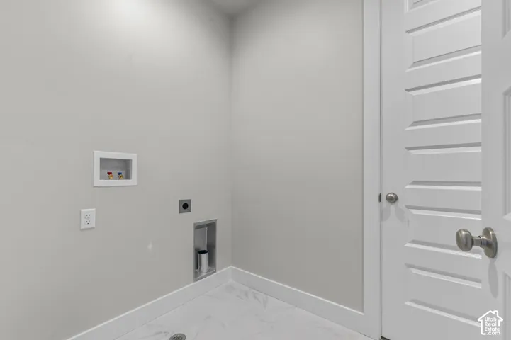 Dedicated utility area featuring white stone-finish tile flooring, a recessed water supply box, an integrated laundry drain, and a multi-panel interior door with a brushed nickel lever