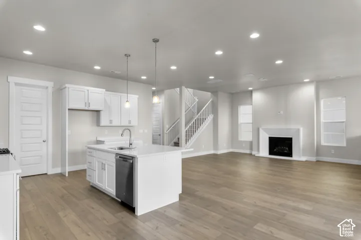 Open-concept interior featuring wood-finish flooring, a kitchen island with stone-surface countertops, recessed lighting, a fireplace with a white mantel, and a staircase with a white balustrade