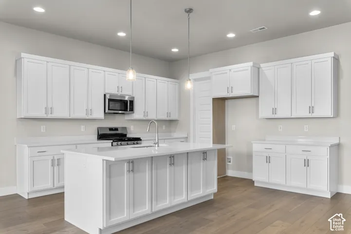 Kitchen featuring white shaker-style cabinetry, a central island with a solid-surface countertop, wood-finish flooring, stainless steel microwave, and pendant lighting