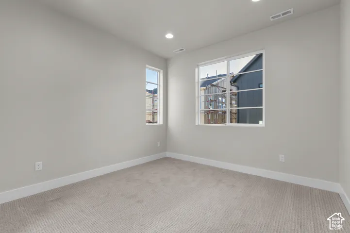 Neutral-toned interior room featuring wall-to-wall carpeting, recessed ceiling lighting, and multiple windows with white frames
