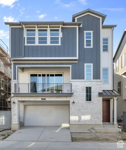 Three-story exterior featuring a mix of vertical siding and stone veneer, a second-story balcony with metal railing, and an attached two-car garage