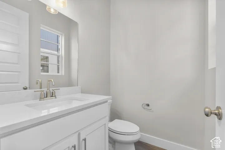 White vanity with a quartz countertop, integrated rectangular sink, dual-handle brushed nickel faucet, large wall-mounted mirror, and wood-finish flooring