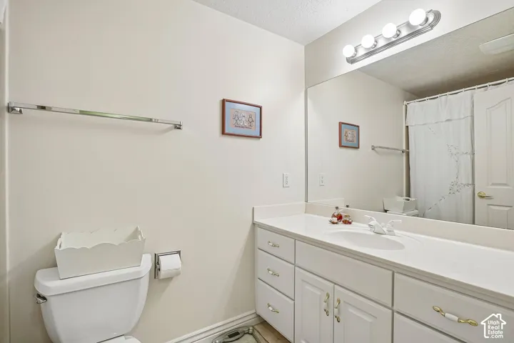 Bathroom featuring a white vanity cabinet with an integrated sink and solid-surface countertop, full-width wall mirror, four-light vanity fixture, and metal hardware