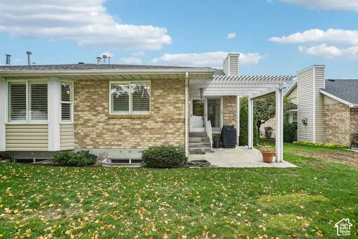 Brick exterior featuring a concrete patio, white wood pergola, and vinyl siding accents