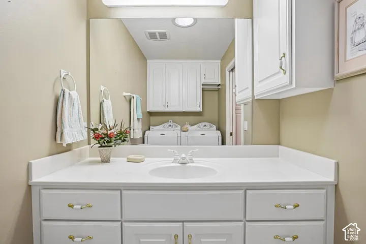 White vanity cabinet with an integrated countertop and sink, large wall-mounted mirror, overhead white cabinetry, and brushed metal hardware