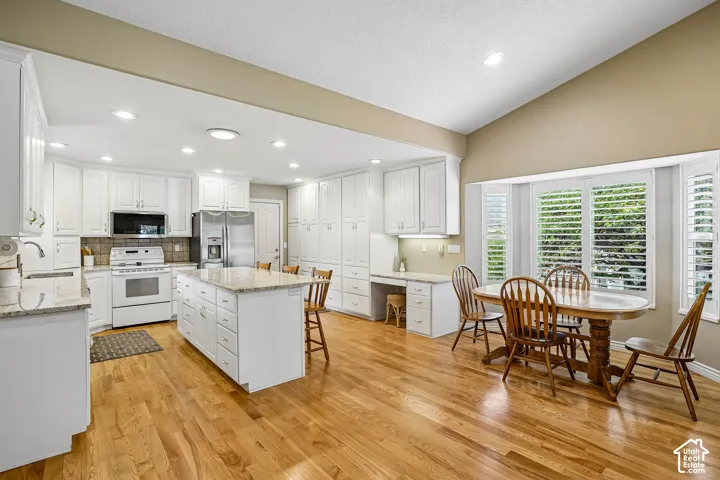 Kitchen featuring white cabinetry, stone-surface countertops, central island, wood-finish flooring, and a recessed bay window with plantation shutters