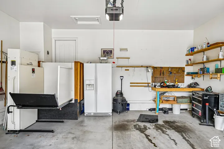 Garage interior featuring a concrete floor, built-in wooden shelving, and a wall-mounted workbench