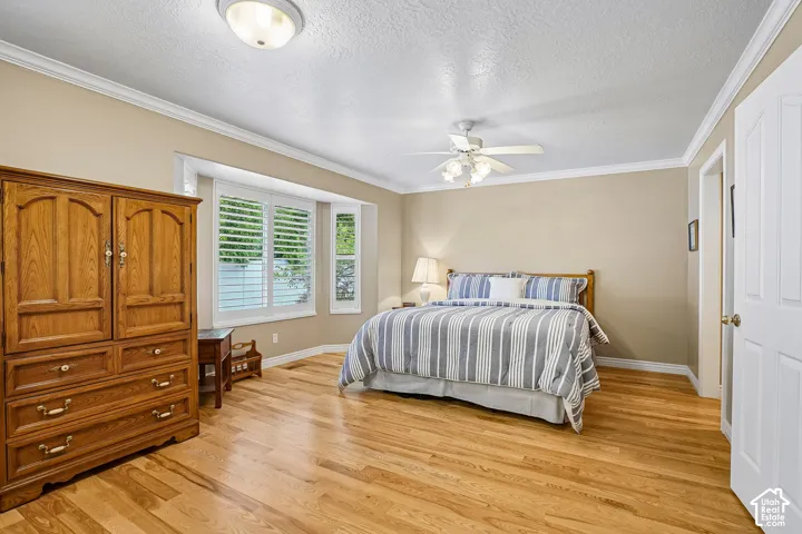 Room featuring wood-finish flooring, crown molding, a bay window with louvered shutters, and a ceiling fan with integrated lighting