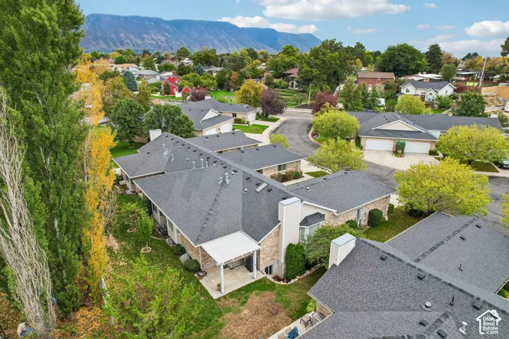 Aerial perspective of a multi-unit property featuring brick masonry, a shingled roof, a covered concrete patio, and a backdrop of mountain scenery