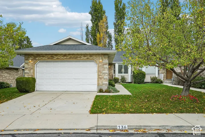 Single-story exterior featuring a brick facade, attached two-car garage, asphalt shingle roof, concrete driveway, and manicured landscaping