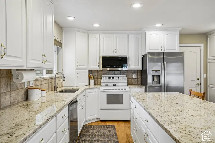 Kitchen featuring white cabinetry, stone countertops, stainless steel refrigerator, stone tile backsplash, and wood-finish flooring