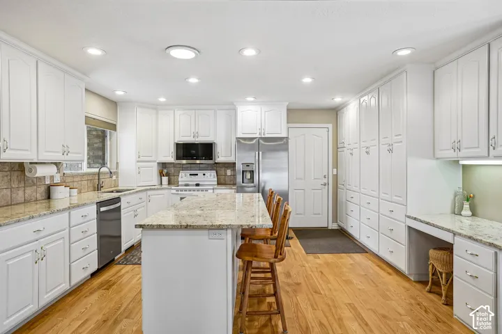 Kitchen featuring white cabinetry, stone countertops, a center island with additional storage, wood-finish flooring, and recessed ceiling lighting
