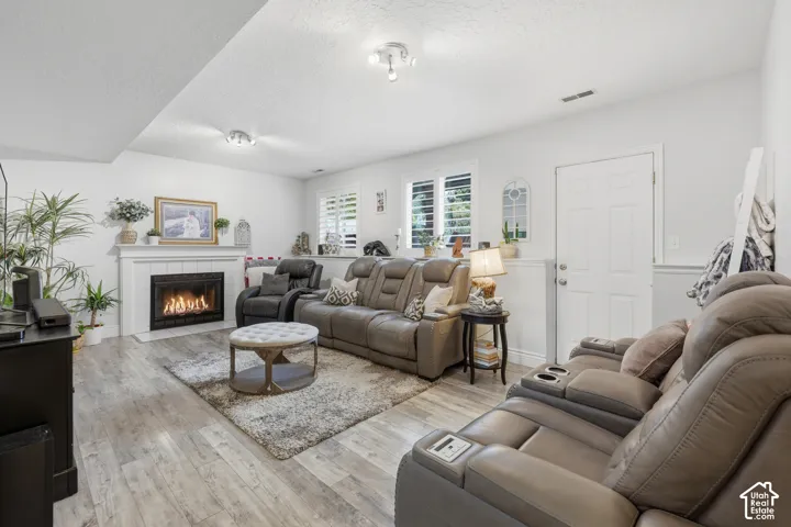 Living area featuring wood-finish flooring, a fireplace with a white mantel, and windows equipped with plantation shutters