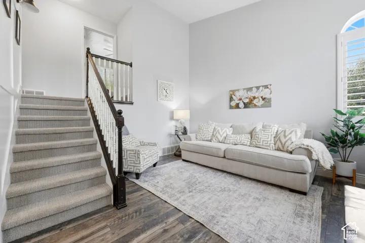 High-ceiling living area featuring wood-finish flooring, staircase with a dark wood handrail and white balusters, and an arched window with plantation shutters