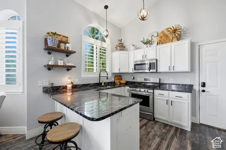 Kitchen featuring white cabinetry, stone countertops, stainless steel appliances, wood-finish flooring, and arched windows with plantation shutters