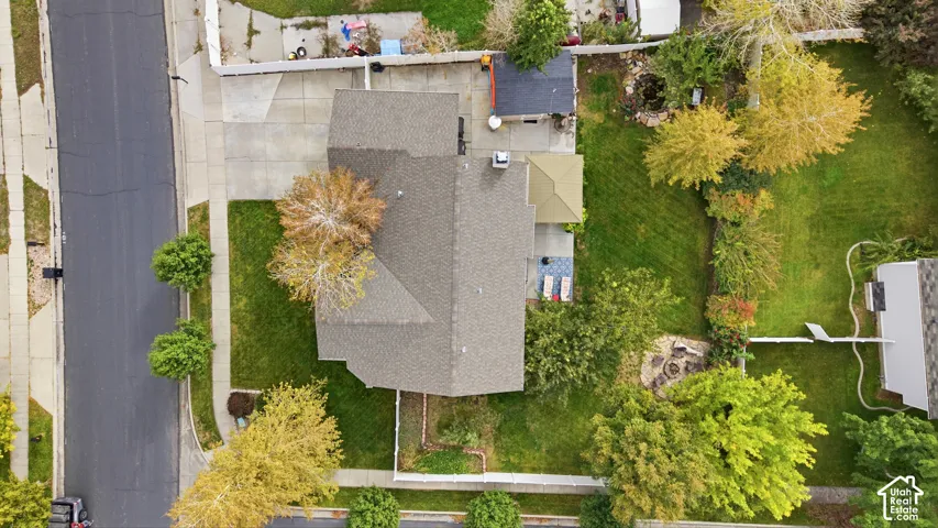 Aerial perspective of property featuring a concrete driveway, paved rear patio, dedicated fire pit area, and landscaped lawn with mature trees
