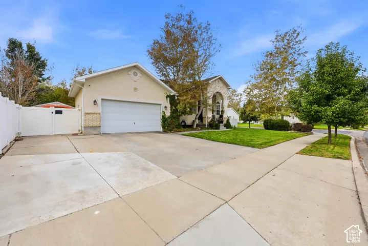 Exterior facade featuring a stucco finish, stone veneer accents, an attached garage, concrete driveway, and white vinyl perimeter fencing