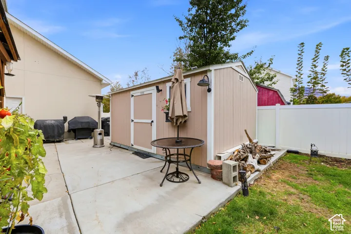 Concrete patio area featuring a detached storage shed, exterior wall-mounted lighting, and white vinyl privacy fencing